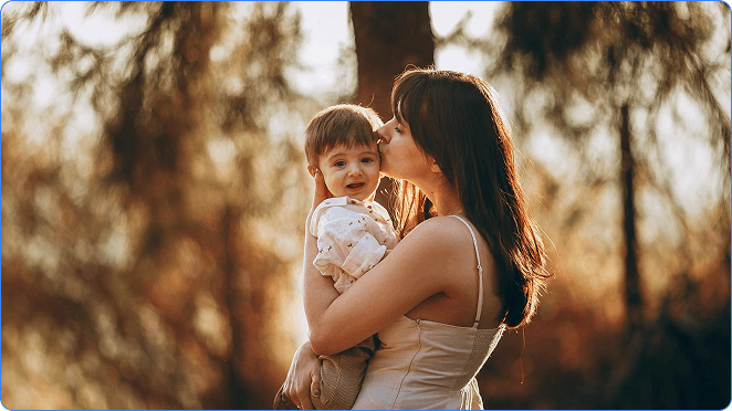 A carer holding a young child outdoors in warm evening light, conveying compassionate support
